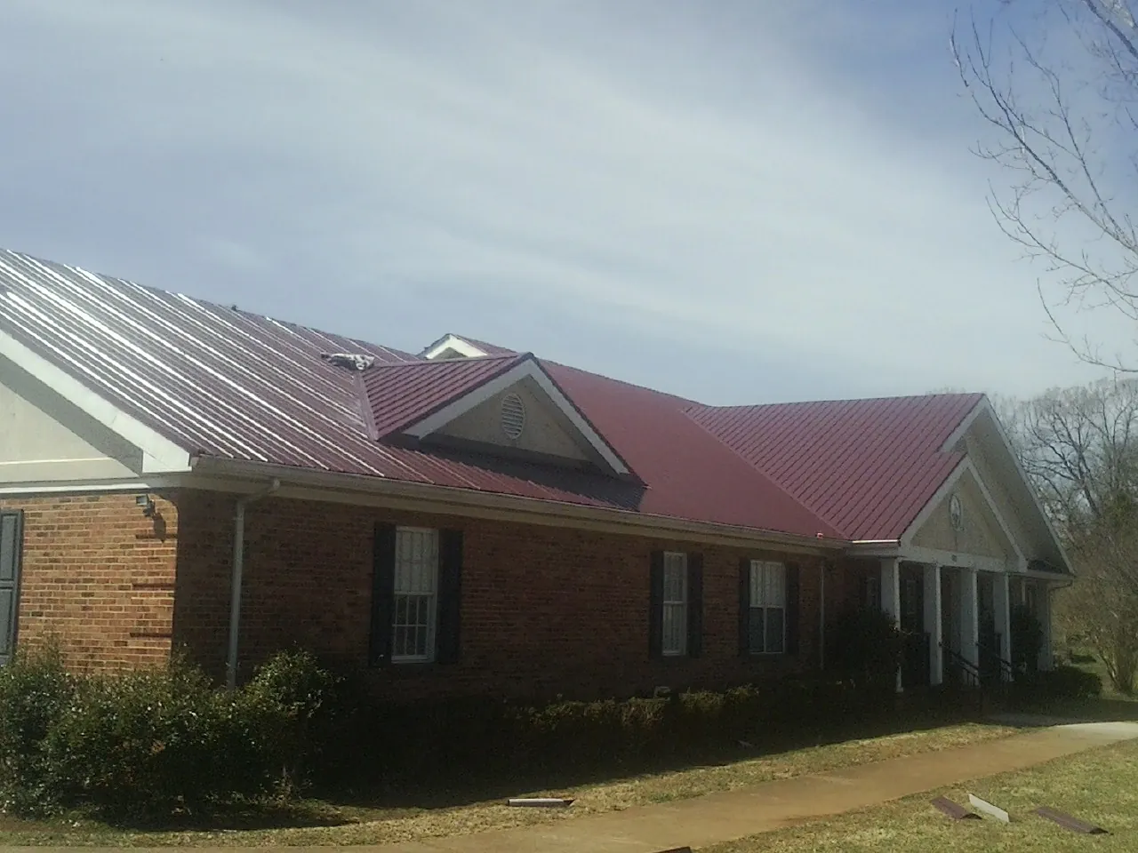 Red metal roof with gabled entries on a long brick building, from a Hail Damage Roof Repair job in Santa Barbara